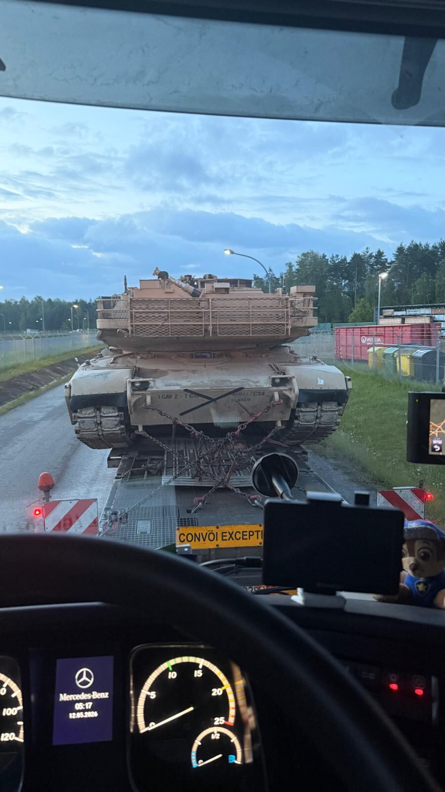 Main battle tank on a trailer seen from the following truck cab at dawn