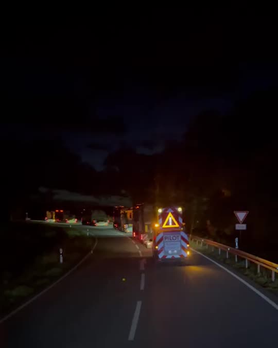 Pilot vehicle with amber warning lights leading a night convoy, seen from the truck cab